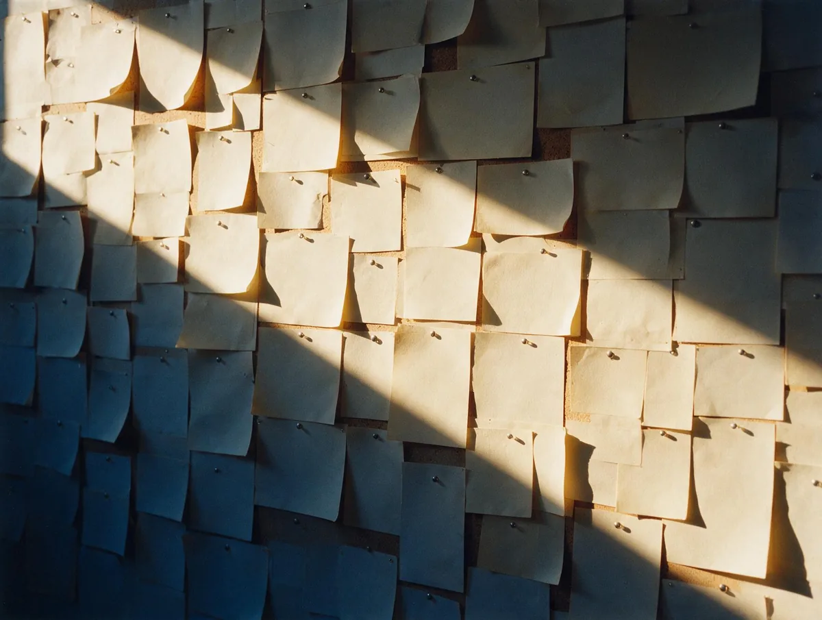A studio wall densely pinned with blank paper proofs in raking light